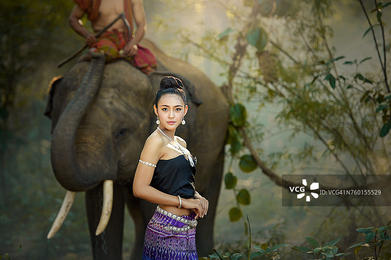 身穿泰国传统服饰的女子与一名驯象员骑着一头大象图片素材