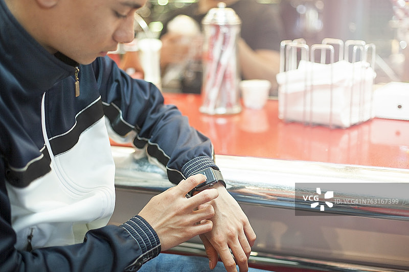 一个年轻人坐在餐厅里，用着智能手表，中段图片素材