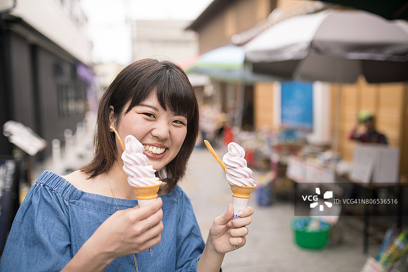 快乐的年轻女人在街上拿着两个冰淇淋图片素材