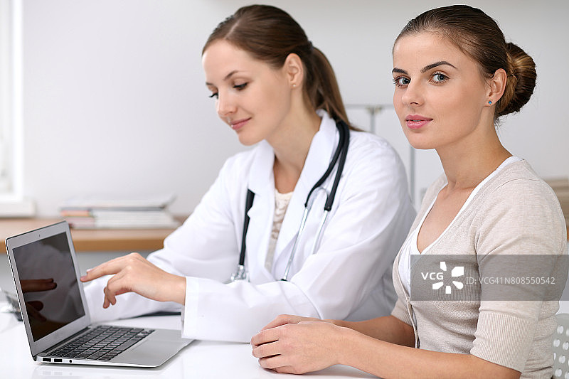 医生和病人坐在桌前。医生指着笔记本电脑。医学保健理念图片素材