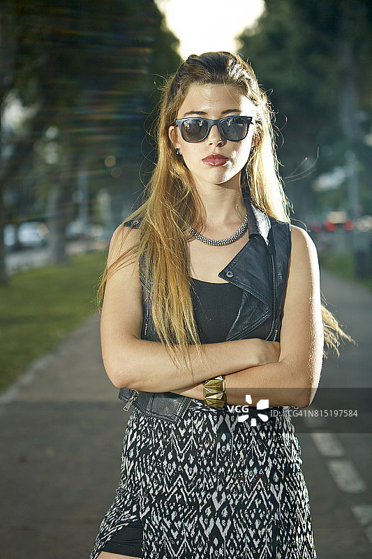 漂亮的女人戴着太阳镜和无袖上衣站在公园白天双臂交叉图片素材