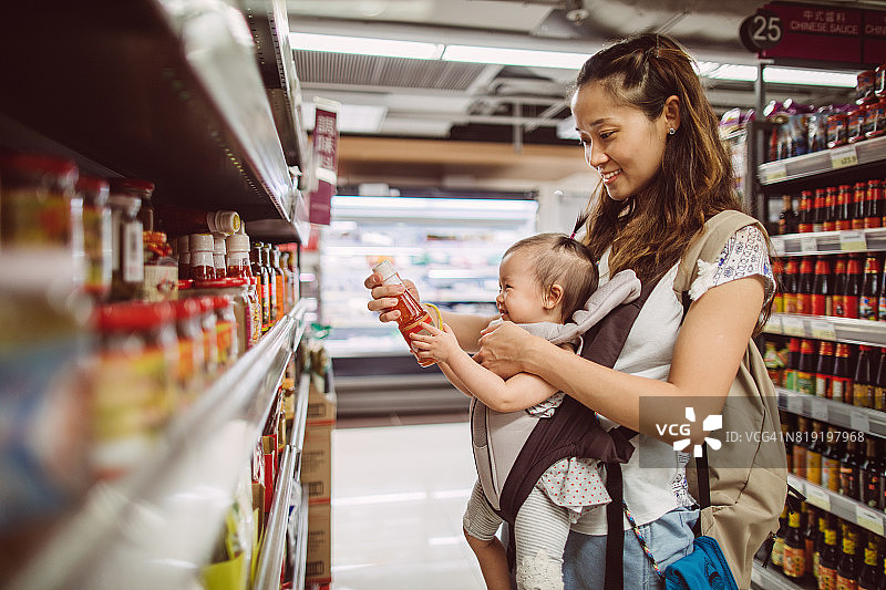 年轻漂亮的妈妈抱着婴儿推车在超市快乐地购物图片素材