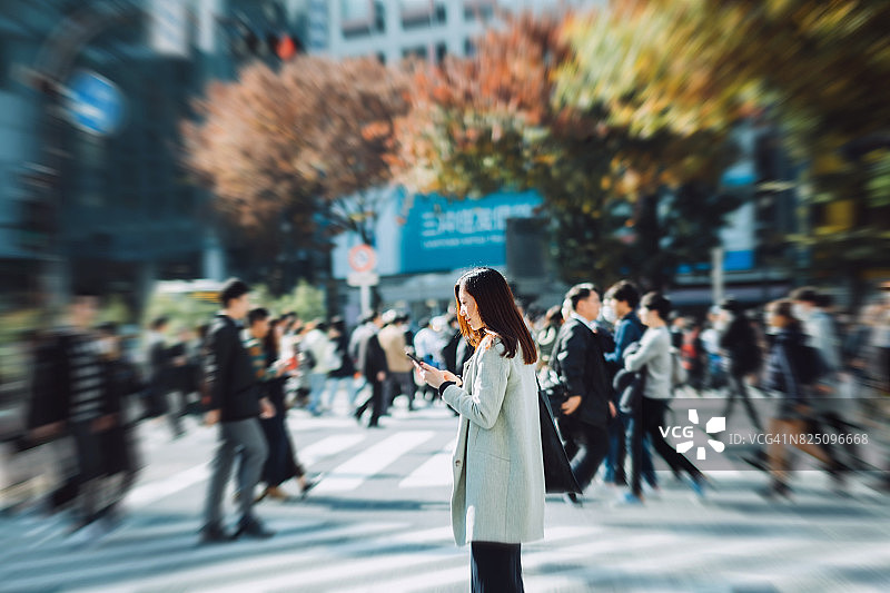 一名年轻女子在过繁忙的城市街道时在人群中使用智能手机图片素材