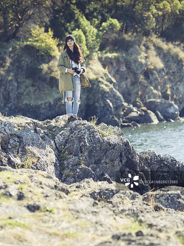 女人拿着相机站在礁石上，背对着蓝色的大海图片素材