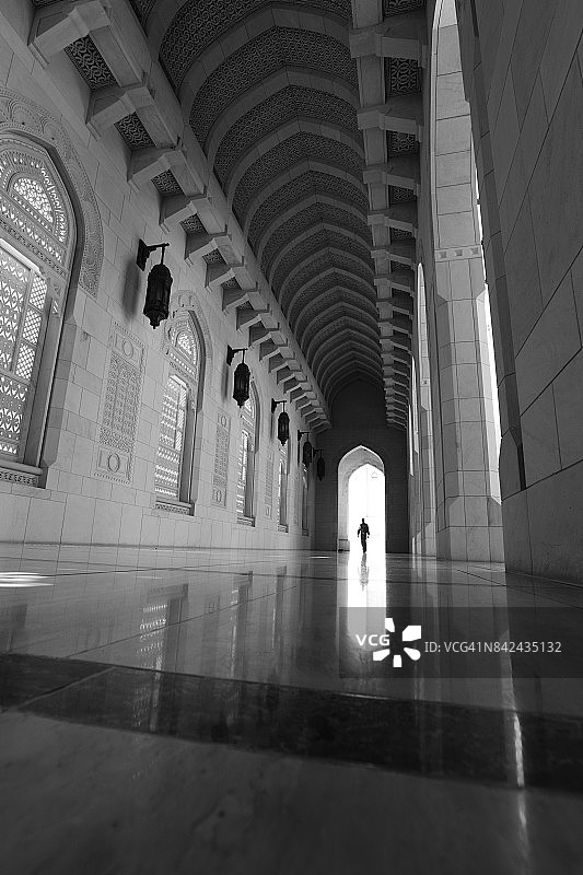 阿曼马斯喀特，一名男子进入苏丹卡布斯大清真寺内院的拱廊图片素材