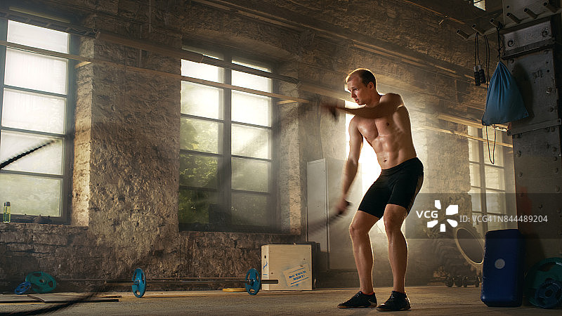在他的交叉健身训练/高强度间歇训练中，肌肉赤裸的男人在健身房用格斗绳练习。图片素材