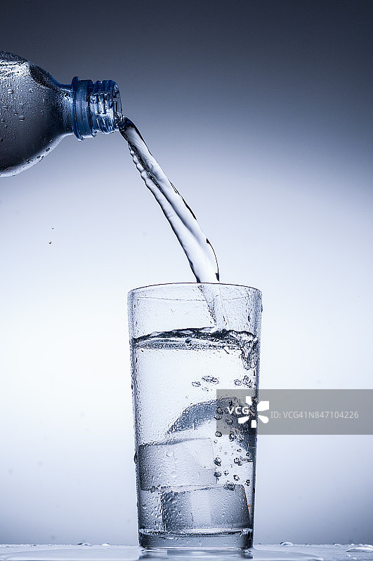 将水从瓶子倒入蓝色背景的玻璃杯中图片素材