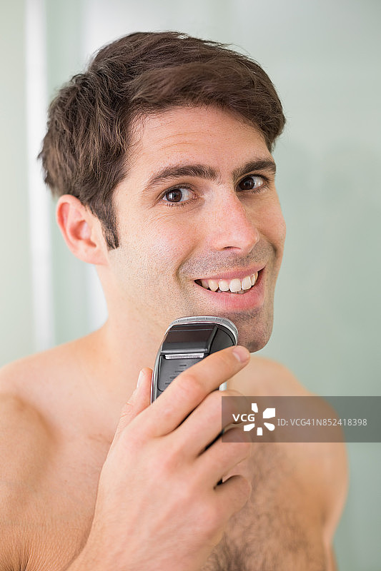 英俊的赤膊男子用电动剃须刀刮胡子图片素材