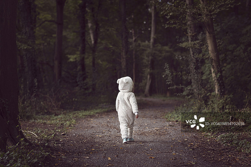 小孩子穿着白熊服，走在林荫小道上图片素材