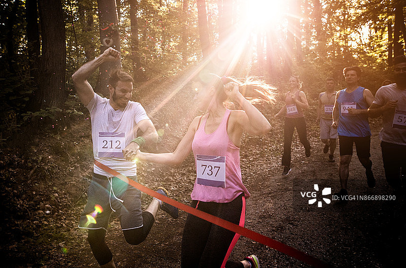 年轻的夫妇微笑着赢得马拉松比赛在森林里，同时跨越终点线在一起。图片素材