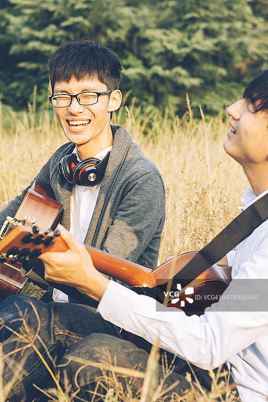 两个男人，朋友坐在草坪上弹吉他图片素材