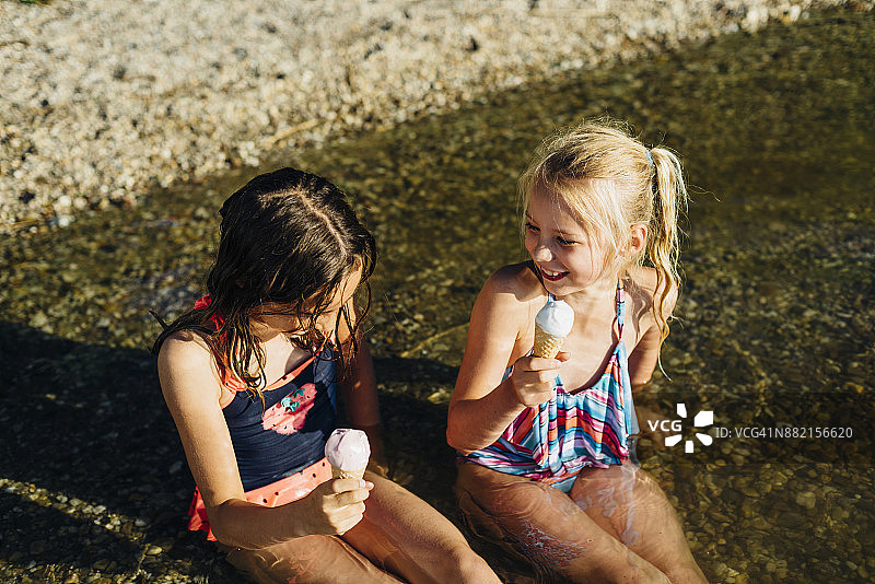 两个女孩坐在湖边的水里吃冰淇淋图片素材