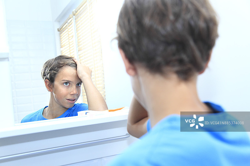 法国，小男孩在浴室里看着镜子里的头发。图片素材