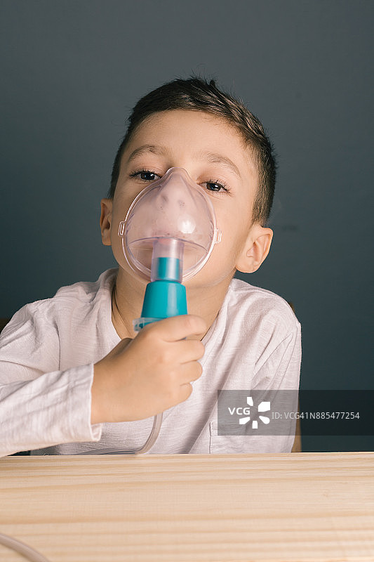 漂亮的病男孩吸入治疗口罩吸入器。一个可爱的小孩患有呼吸道疾病或哮喘。从氧气面罩看带有烟雾的喷雾器。图片素材