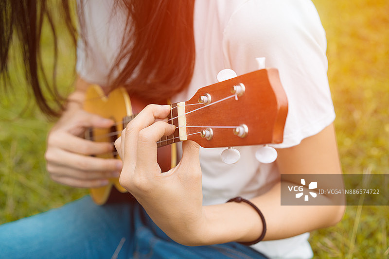 女孩在花园里弹奏尤克里里与原声吉他的特写，年轻女子演奏音乐的生活方式经典图片素材