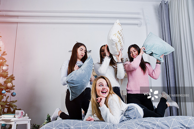 四个可爱的朋友女孩穿着暖和的毛衣和黑色的裤子在床上的工作室装饰房间新年。图片素材