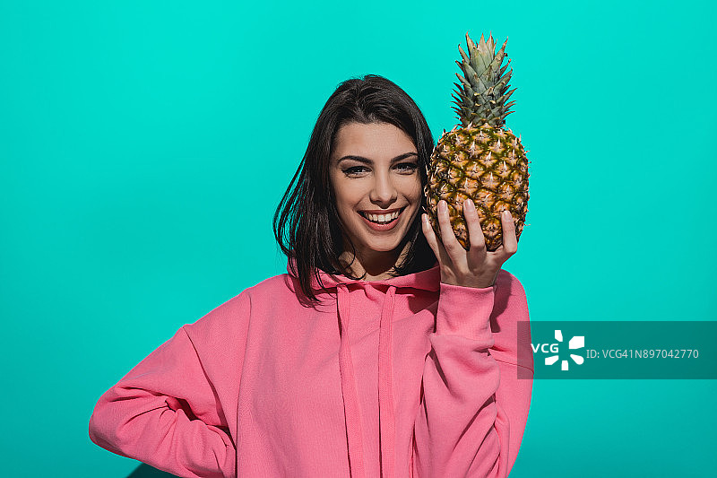 一个年轻女子拿着一个菠萝，站在一个蓝色的背景图片素材
