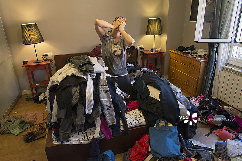 在一间凌乱的卧室里，一个女人在一堆衣服间哭泣的肖像图片素材
