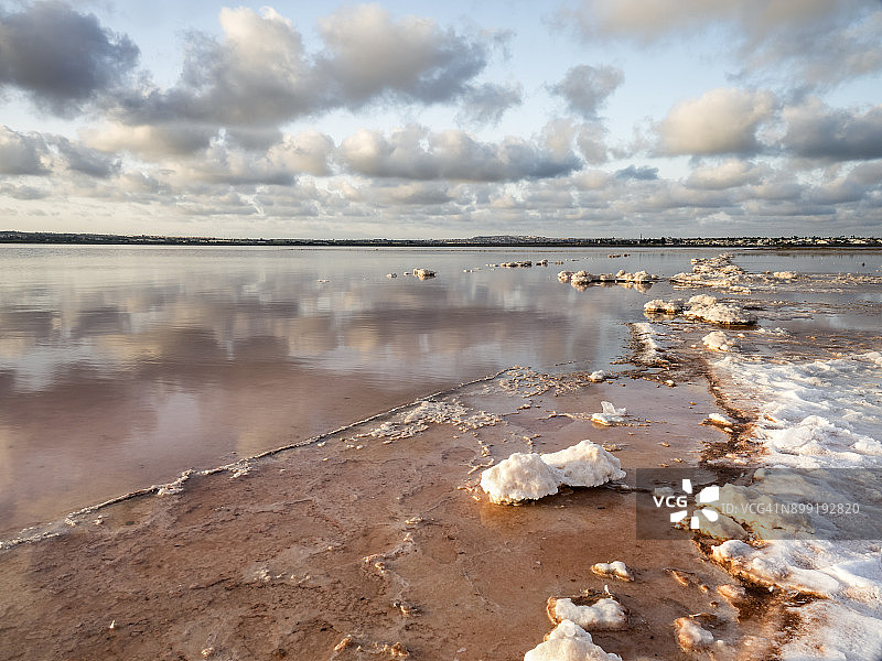 在西班牙托雷维耶哈(巴伦西亚社区)的盐矿里，把橙色的太阳放在咸水的泻湖里，他的海岸被盐的纹理和形式覆盖着。图片素材
