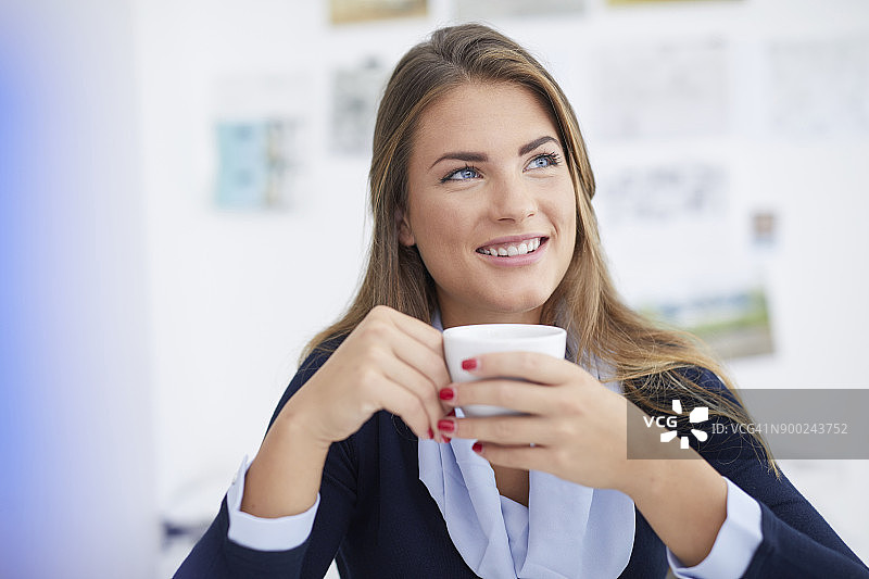 微笑的年轻女子正在办公室喝咖啡休息图片素材