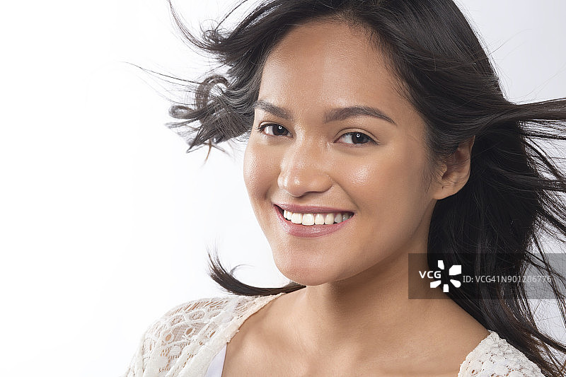 一个年轻快乐的亚洲女士的肖像，穿着白色上衣，在一个工作室的背景，风吹过她的头发图片素材