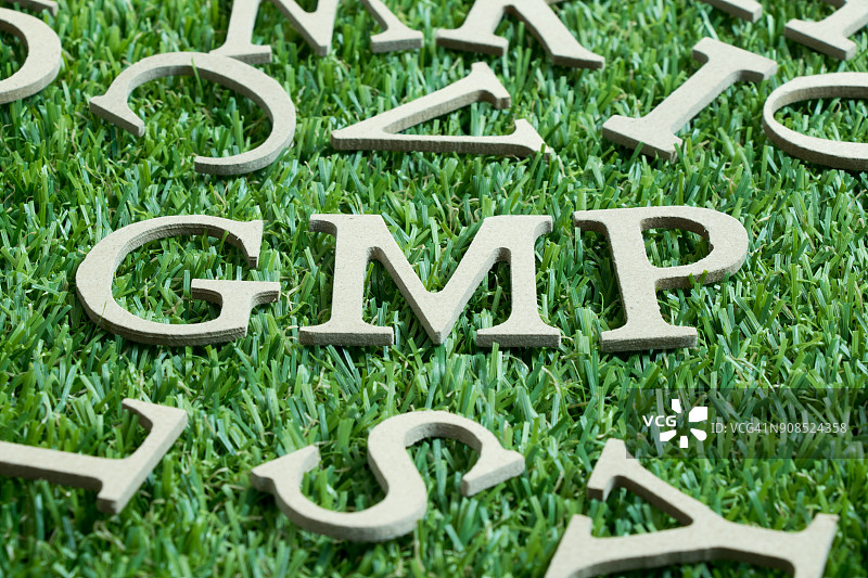 木质字母字GMP(源自良好生产规范的缩写)上人工绿草配英文字母为背景图片素材