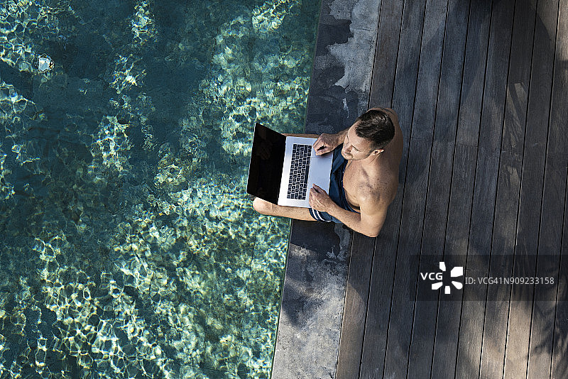 一个成熟的男人坐在泳池边，用着笔记本电脑图片素材