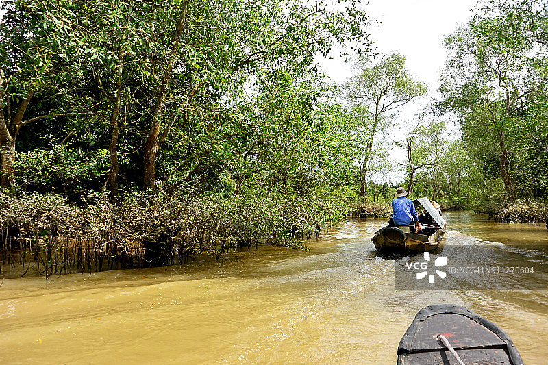 越南湄公河三角洲运河上，锡顶摩托艇正驶过一艘木制划艇图片素材