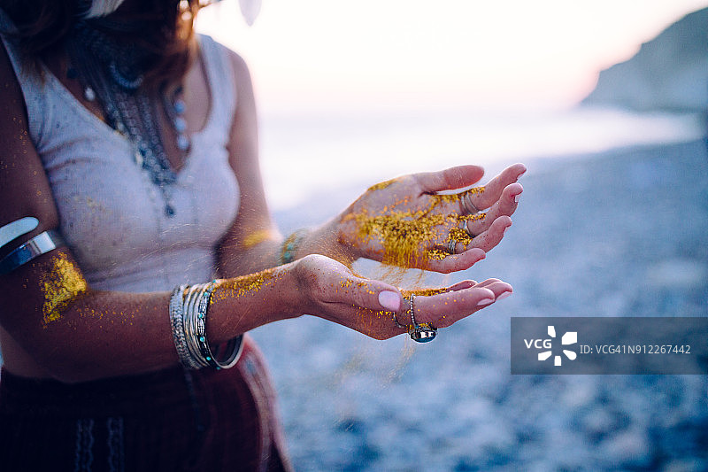 海滩上的波西米亚女人，手上带着金色的闪光图片素材