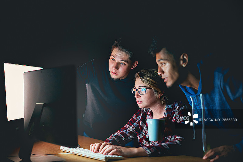 三个年轻人在晚上聚精会神地盯着电脑图片素材