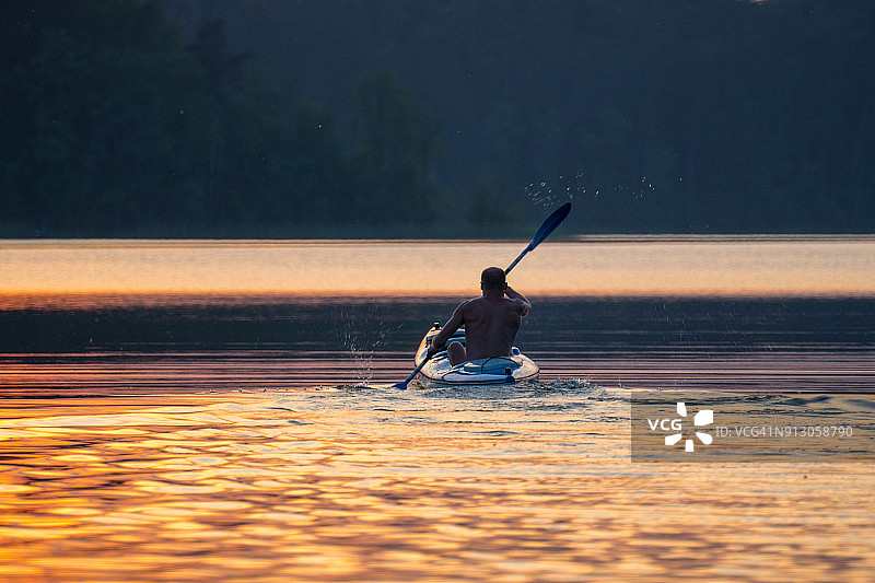 夏天放松活动。一个年轻人在湖上划皮艇。日落图片素材