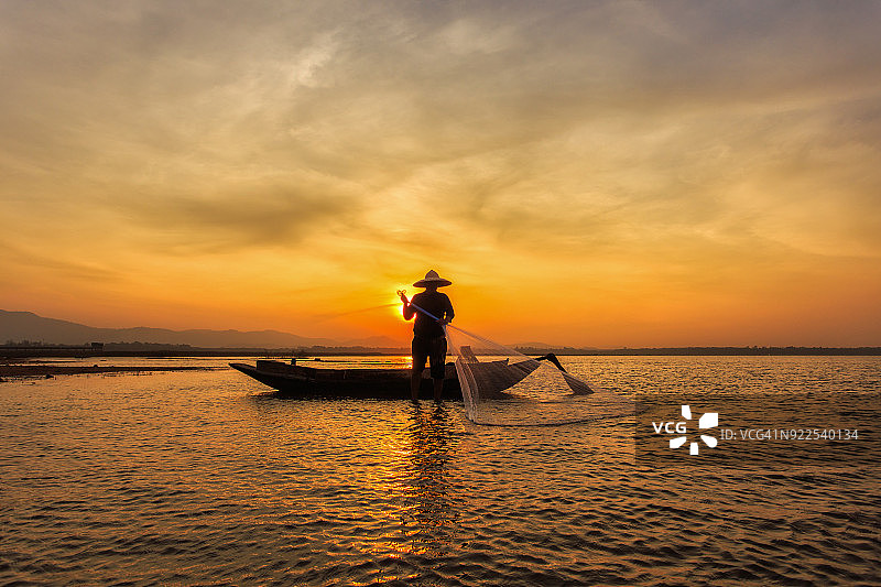 日落时分，湖面上的小船上坐着一位渔夫图片素材