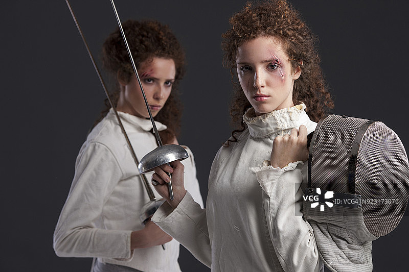 击剑运动的竞争。决斗。深灰色背景。运动的女人。一对红头发的双胞胎女孩，击剑运动员。双胞胎。图片素材