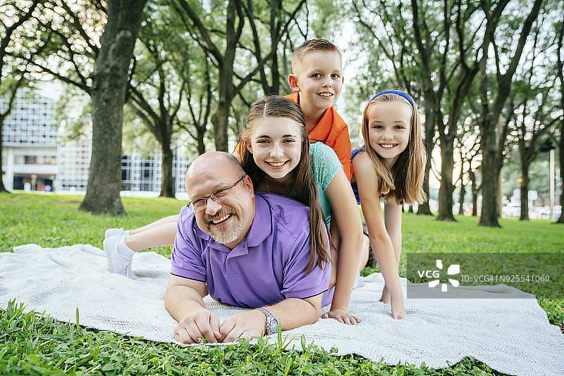 在公园里，白人男孩和女孩躺在父亲的背上图片素材