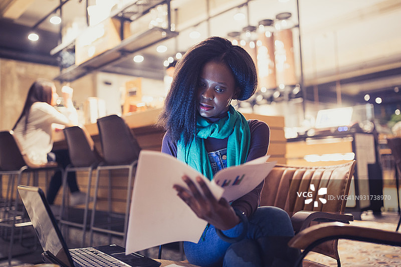 一位非洲裔美国年轻女性，在咖啡馆的咖啡休息时间，用笔记本电脑工作，浏览文档图片素材
