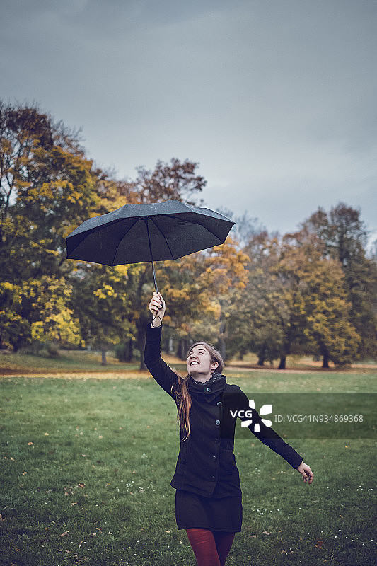 快乐的年轻女子与伞在秋天的公园跳舞图片素材