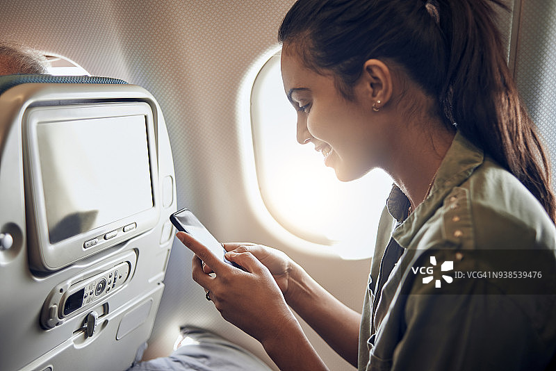 漂亮的年轻女子在飞机上用她的智能手机图片素材
