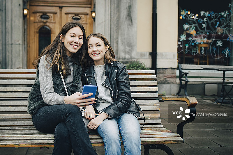 微笑的女性朋友与手机坐在长凳上的肖像图片素材
