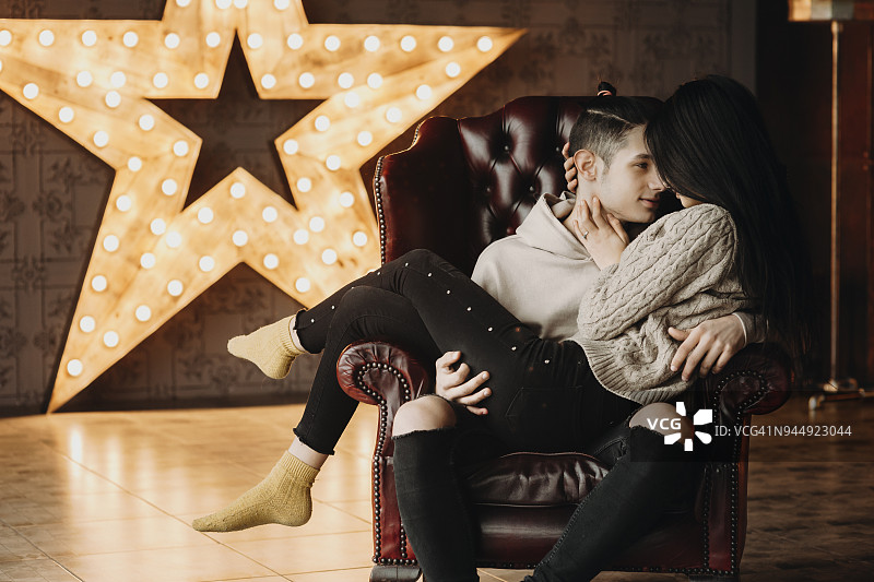 一对舒适的夫妇坐在皮椅上，男孩抱着他的女朋友，看着对方，而在他们的背后有一个大明星在发光。图片素材