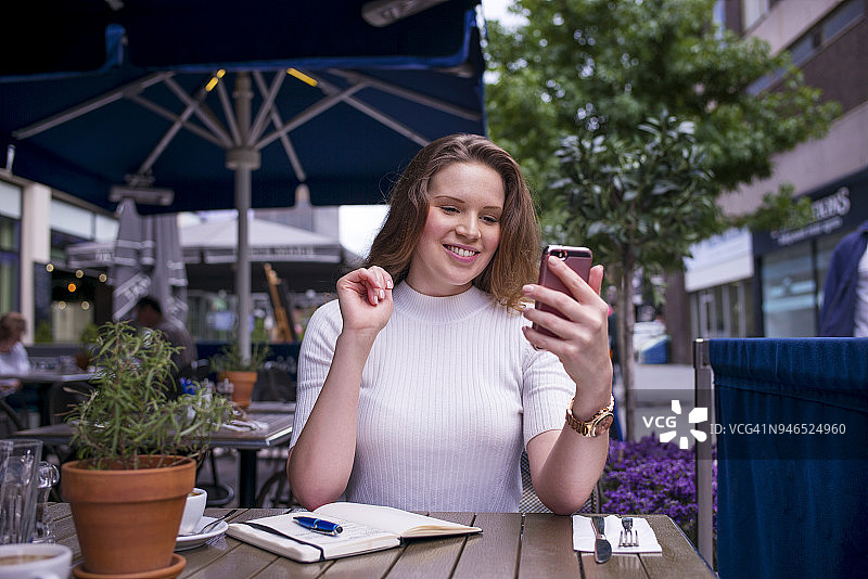 一名年轻女子坐在咖啡馆外面查看手机图片素材