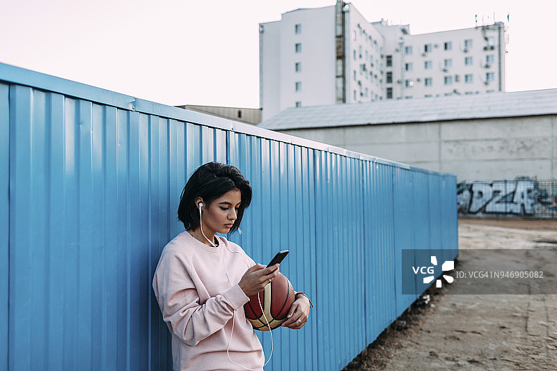 在集装箱里拿着篮球、智能手机和耳机的年轻女子图片素材