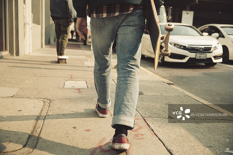 在人行道上走着滑板的男人的低部分图片素材