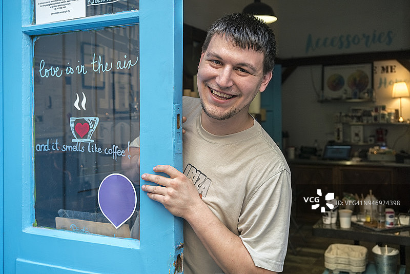咖啡烘焙工坊门上微笑的咖啡烘焙师的肖像图片素材