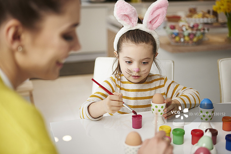 妈妈和女儿带着兔耳朵坐在桌子旁画复活节彩蛋图片素材