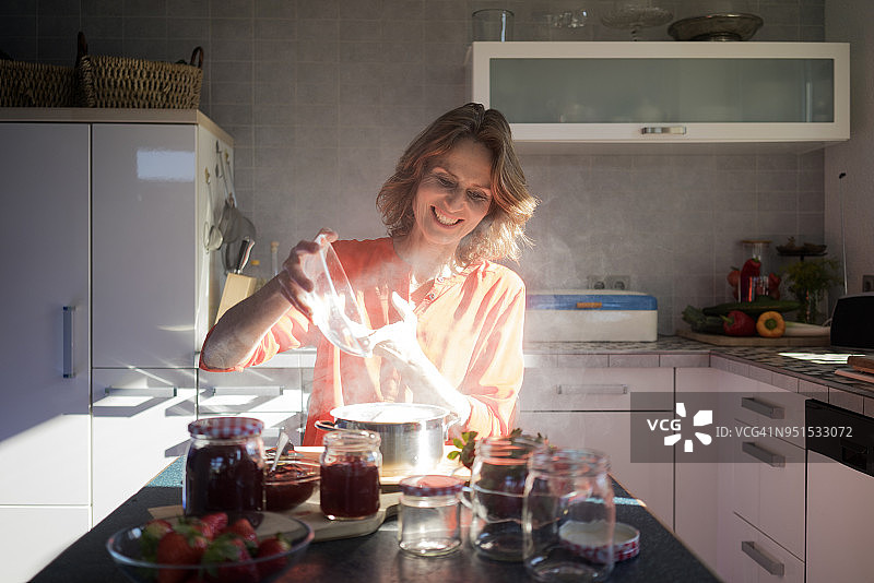 微笑的女人在厨房里做草莓酱图片素材
