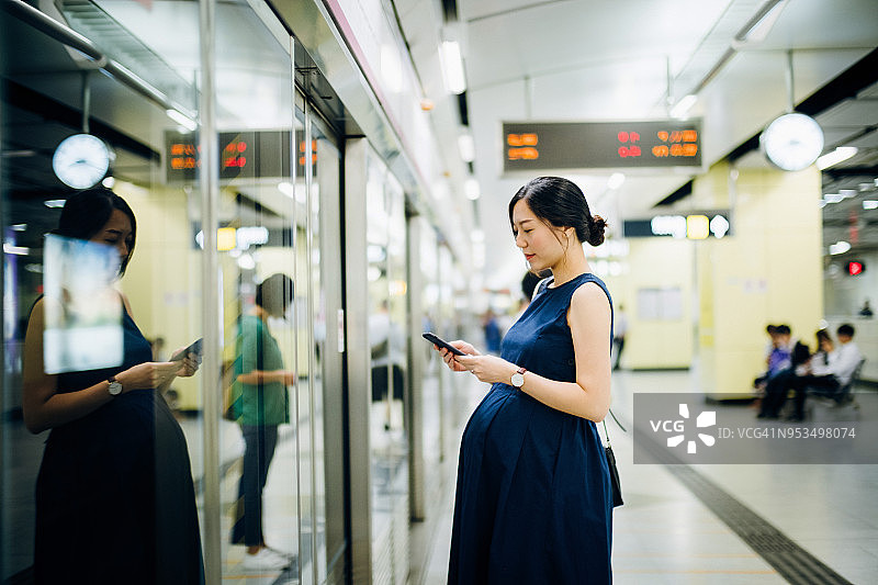 美丽的孕妇在站台上等车时使用智能手机图片素材