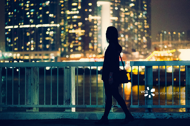 夜晚，一个女人的剪影走过码头，俯瞰着城市的景色图片素材