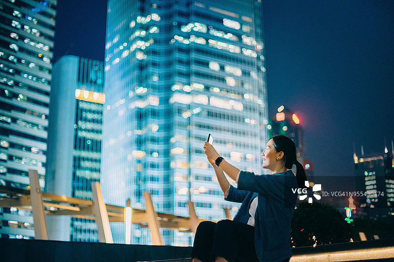 年轻的女游客在市中心用智能手机捕捉城市夜景图片素材