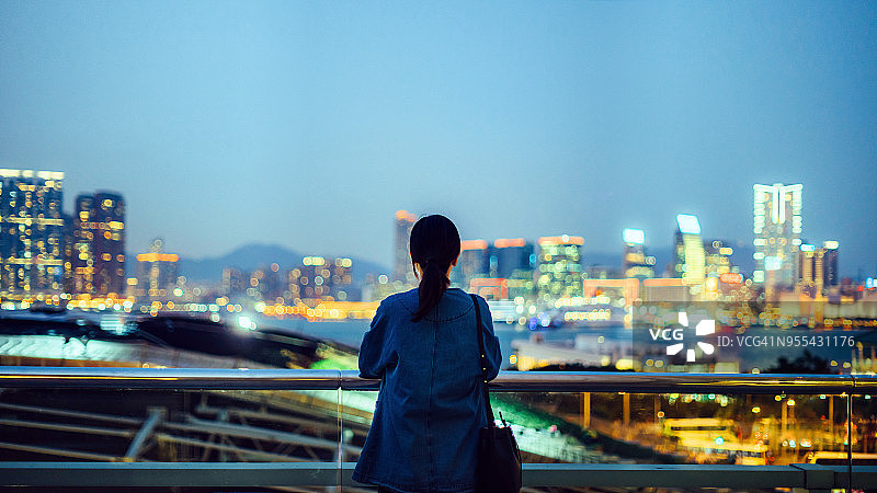 女人的后视图站在屋顶阳台俯瞰壮观的城市天际线在黄昏图片素材