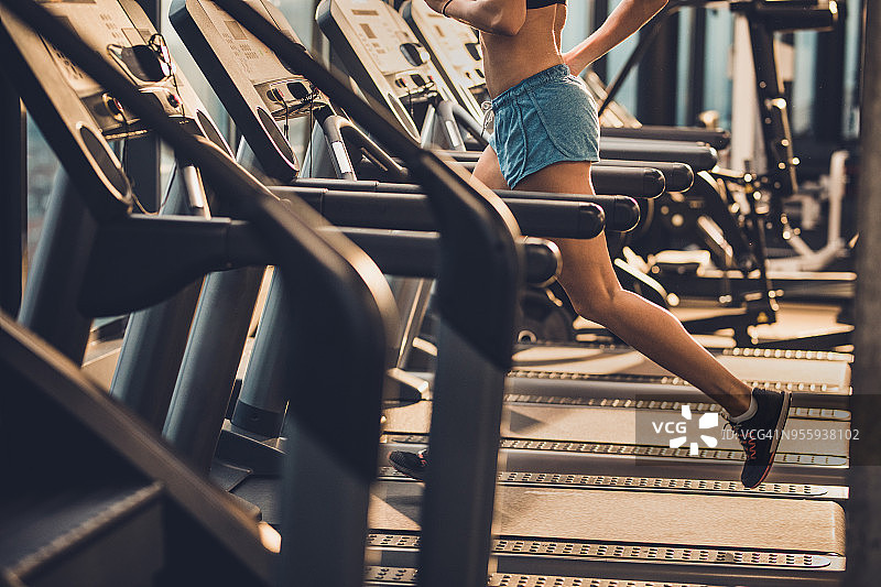 一个不知名的运动女人在跑步机上热身在一个健康俱乐部。图片素材